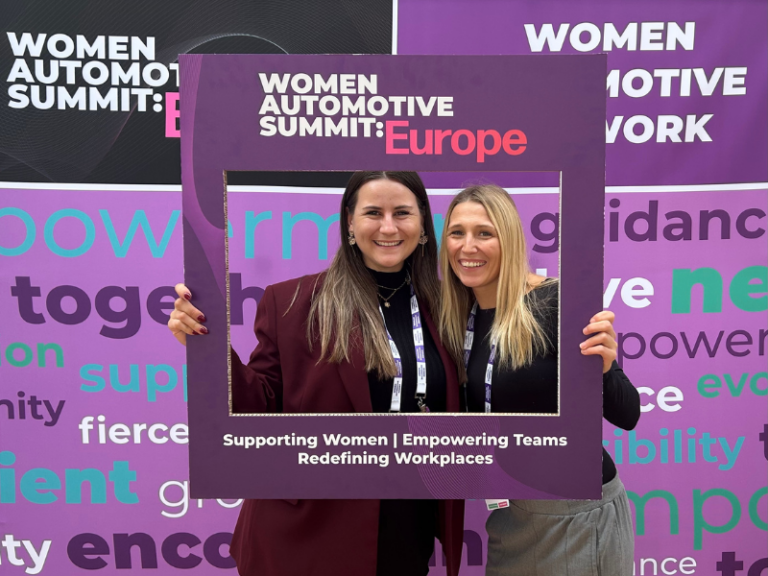 Zwei Frauen beim Women Automotive Summit Europe lächeln vor einem Rahmen mit Botschaft zur Förderung von Frauen und Vielfalt in der Automobilbranche